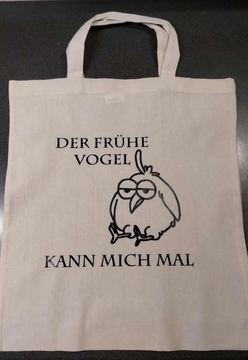 Könnte beinhalten: Eine weiße Einkaufstasche mit schwarzem Text und einem Comic-Vogel. Der Text lautet "Der frühe Vogel kann mich mal".