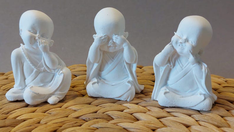 Könnte beinhalten: Drei weiße Figuren von Personen mit verbundenen Augen, jede mit den Händen, die ihre Augen bedecken. Die Figuren sitzen in einer entspannten Pose mit gekreuzten Beinen. Die Figuren sind aus einem glatten, weißen Material gefertigt und haben ein schlichtes, elegantes Design.