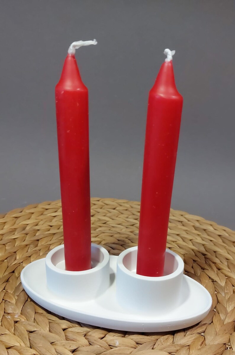Könnte beinhalten: Zwei rote Kerzen in einem weißen Kerzenhalter aus Keramik. Der Halter hat zwei separate Fächer für die Kerzen.