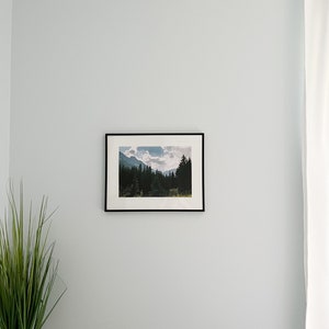 Peut inclure: Une photographie en noir et blanc encadr&eacute;e d'une cha&icirc;ne de montagnes avec une for&ecirc;t au premier plan. La photo est accroch&eacute;e &agrave; un mur bleu clair.