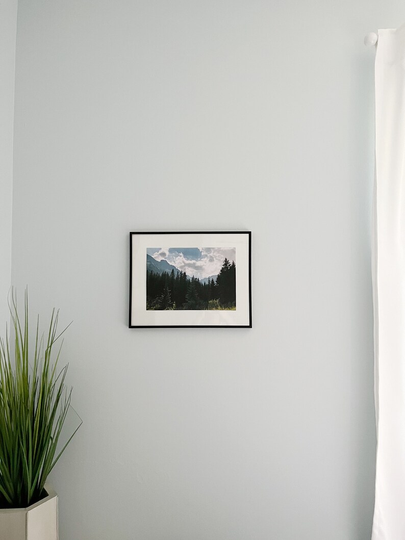 Peut inclure: Une photographie en noir et blanc encadr&eacute;e d'une cha&icirc;ne de montagnes avec une for&ecirc;t au premier plan. La photo est accroch&eacute;e &agrave; un mur bleu clair.