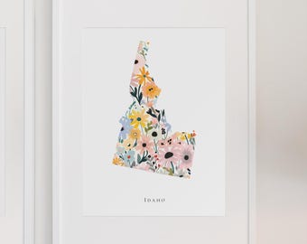 May include: A framed print featuring the state of Idaho filled with a floral pattern. The flowers are in shades of pink, yellow, blue, and white. The word "Idaho" is printed in a simple font below the state outline.