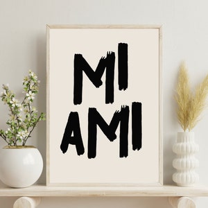 Peut inclure: Une impression encadr&eacute;e avec le texte "MI AMI" en lettres noires en forme de coups de pinceau sur un fond blanc.