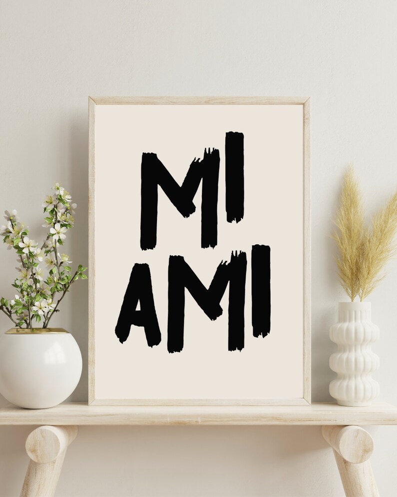 Peut inclure: Une impression encadr&eacute;e avec le texte "MI AMI" en lettres noires en forme de coups de pinceau sur un fond blanc.