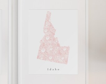 May include: A white framed print of the state of Idaho with a pink floral pattern. The print has the word "Idaho" written below the state outline.