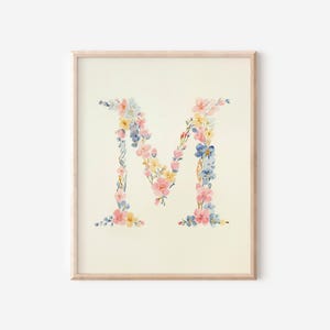 Könnte beinhalten: Gerahmter Druck mit dem Buchstaben "M", der aus Aquarellblumen in Rosa, Gelb und Blau besteht. Das florale Design ist vor einem cremefarbenen Hintergrund platziert und in einem hellen Holzrahmen eingefasst, ideal für die Inneneinrichtung.