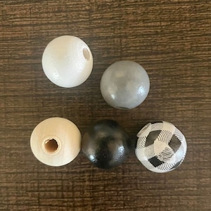 May include: Five wooden beads in different colours and patterns. The beads are white, grey, black, and black and white chequered.