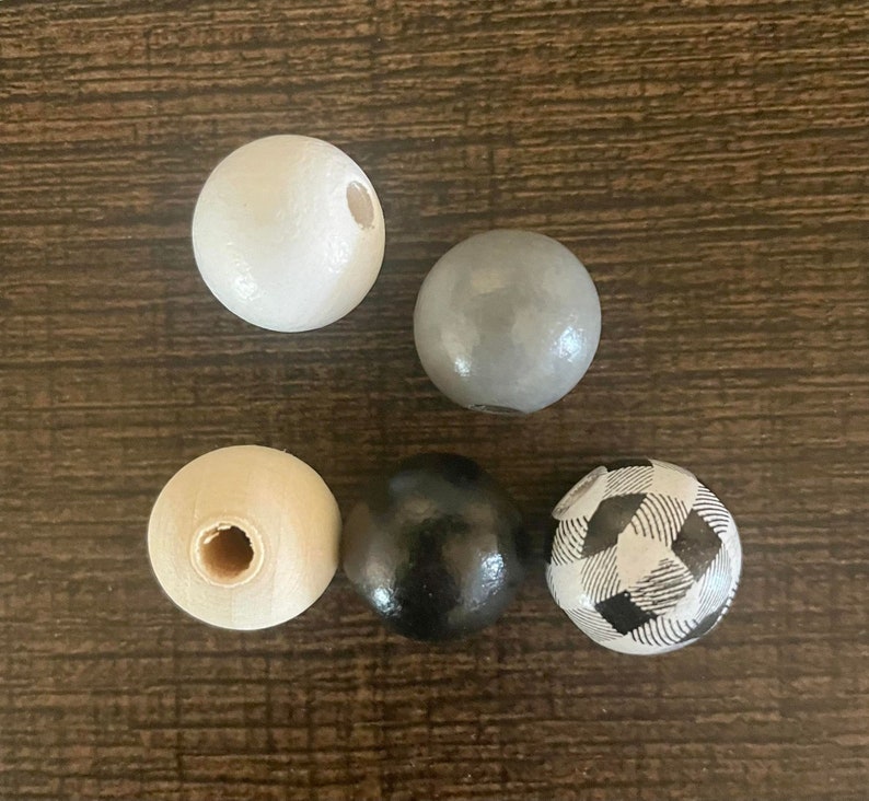 May include: Five wooden beads in different colours and patterns. The beads are white, grey, black, and black and white chequered.