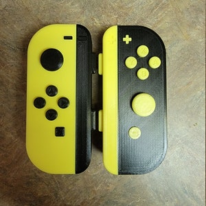 Peut inclure: Une paire de manettes Joy-Con Nintendo Switch jaunes et noires. La manette gauche Joy-Con a une face avant noire et la manette droite Joy-Con a une face avant noire avec des boutons jaunes.