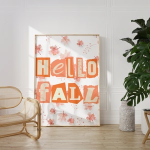 Puede incluir: Una impresión enmarcada con fondo blanco y un mensaje "hello fall" de color melocotón con hojas de color melocotón esparcidas alrededor del texto.