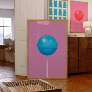 Può includere: Una stampa d'arte astratta rosa e blu con un grande lecca-lecca blu su un bastoncino bianco. Il lecca-lecca è su uno sfondo rosa con una nuvola bianca nell'angolo in alto a sinistra.