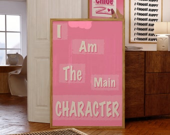 May include: Pink and white motivational poster with the text "I Am The Main Character" in a bold, white font. The poster is framed in a light wood frame.