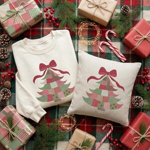 May include: A cream-colored crewneck sweatshirt and a square throw pillow, both featuring a graphic of a patchwork-style Christmas tree topped with a red bow. The tree design consists of various green, red, and pink patterned squares.