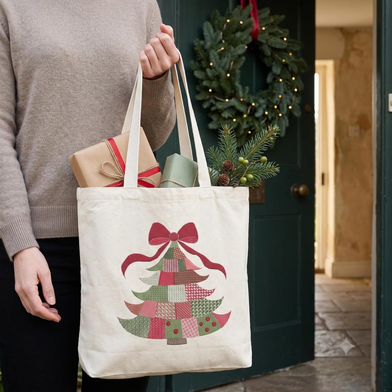 May include: A cream-colored canvas tote bag featuring a graphic of a Christmas tree made of various red and green patterned patches, topped with a large red bow. The bag contains wrapped gift boxes and a small sprig of evergreen foliage.