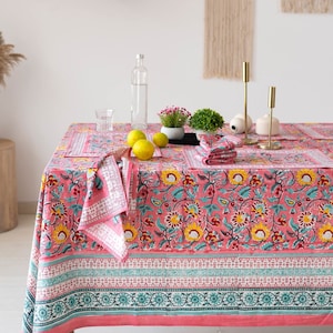 Puede incluir: Un mantel de mesa rosa con estampado floral y borde verde. El mantel está puesto sobre una mesa con limones, flores y candelabros.
