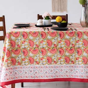 Puede incluir: Un mantel amarillo con un patrón floral en tonos rosa y verde. El mantel tiene un borde rojo y un borde estampado blanco y azul.