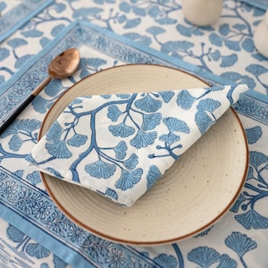 Puede incluir: Una servilleta de algod&oacute;n con estampado azul y blanco doblada sobre un plato blanco con borde marr&oacute;n. El plato est&aacute; sobre un mantel con estampado azul y blanco.