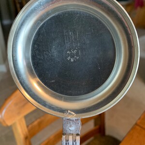 May include: Close-up of the lid of a silver beer stein with a hinged lid. The lid has a circular, embossed design and the inscription "ZINN 90/80" in the center.