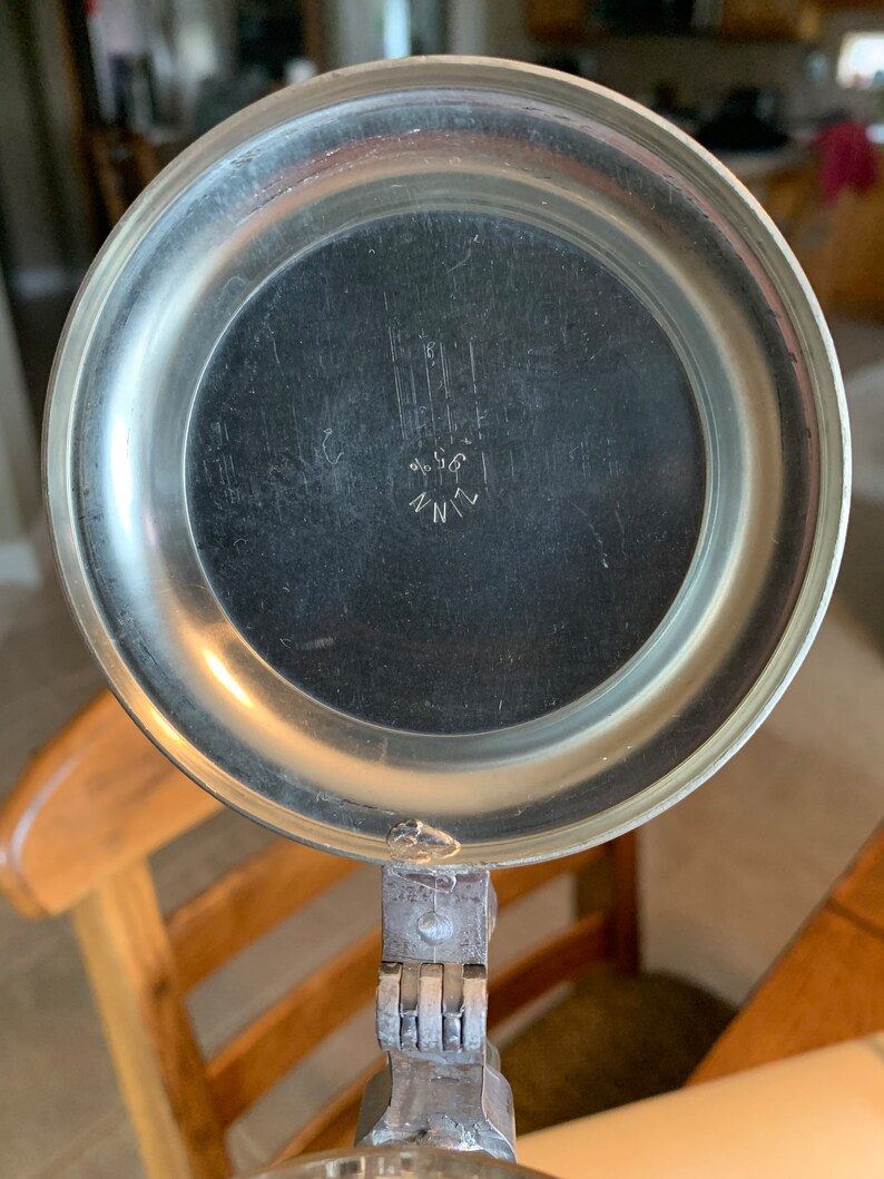May include: Close-up of the lid of a silver beer stein with a hinged lid. The lid has a circular, embossed design and the inscription "ZINN 90/80" in the center.