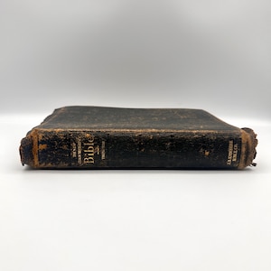 May include: A well-worn, antique Bible with a dark cover. The spine and edges show signs of age and wear. Gold lettering on the spine reads "The New Chain Reference Bible" and "Thompson". The book is from the B.B. Kirkbride Bible Co.