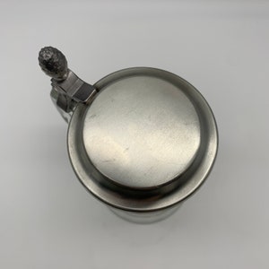 May include: A silver pewter beer stein with a lid and a hinged handle. The lid has a small, round knob on top.