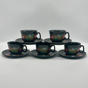 May include: Set of six black teacups and saucers with a floral design in red, yellow, and white. The cups and saucers have a glossy finish.