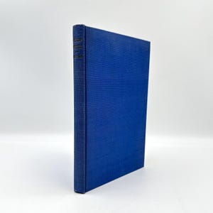 May include: A hardcover book with a textured, deep blue cover. The spine features text in a contrasting color. The book is standing upright against a white background. The book's cover has a subtle, woven pattern.