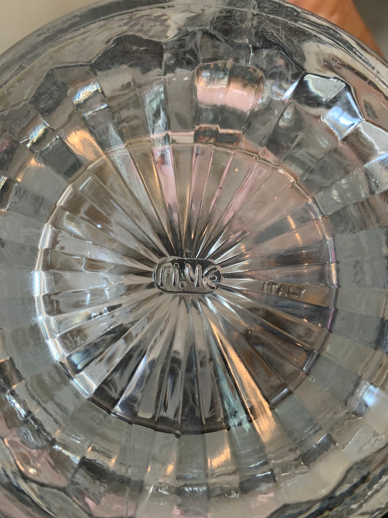 May include: Close-up of the bottom of a clear glass pitcher with a textured surface. The bottom of the pitcher has a circular label that reads "Fi.Me" and "ITALY".