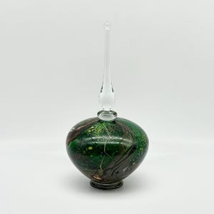 May include: A decorative glass bottle with a clear, elongated stopper. The bottle's body is a vibrant green with brown and yellow swirls, and a textured pattern. The base is a dark color, and the stopper is clear glass.