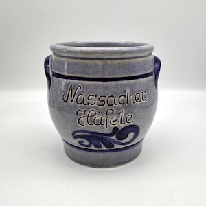 May include: A blue-gray ceramic jar with two handles and the text "Nassacher Häfele" in dark blue script. The jar has a dark blue band around the middle and a decorative swirl design.
