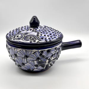 May include: A blue and white ceramic soup bowl with a lid and handle. The bowl features a floral design and a textured lid with a dark blue knob. The handle is also dark blue.