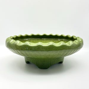 May include: A green ceramic bowl with a scalloped rim and three small feet. The bowl has a speckled texture and a glossy finish. The bowl is a shade of green.