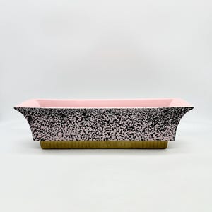 May include: A rectangular ceramic planter with a speckled black and white glaze. The planter has a pink interior and a gold-colored base.