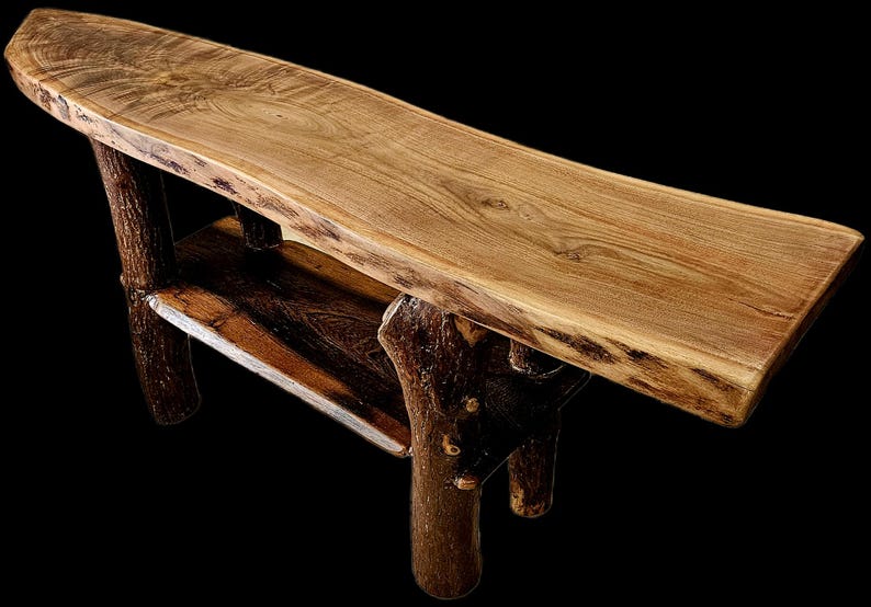 May include: A rustic wooden bench with a natural edge, featuring a light brown tabletop and dark brown, branch-like legs. The bench has a lower shelf and is made of solid wood. The design is reminiscent of a natural, organic aesthetic.