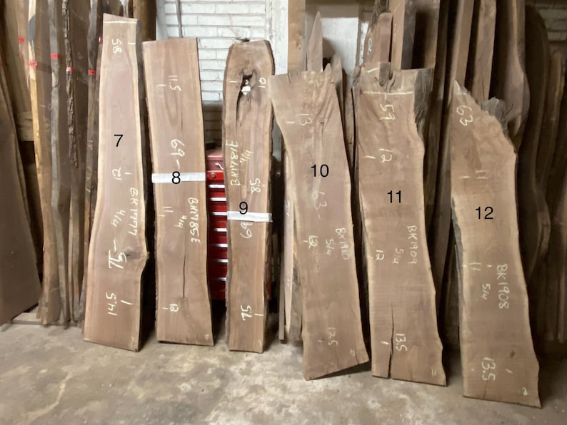 May include: A collection of rough-cut, unfinished wood slabs, each with a unique shape and natural edge. The slabs vary in width and length, with handwritten measurements in inches. The wood has a warm, brown tone, ideal for woodworking projects.