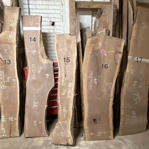May include: A collection of raw, unfinished wood slabs of varying sizes and shapes. The slabs are light brown with natural edges and visible grain. Measurements are written on the slabs in inches. Ideal for woodworking projects.