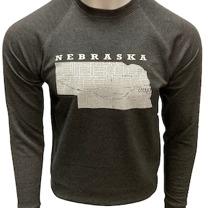 May include: A dark gray long-sleeved sweatshirt with a white outline of the state of Nebraska. The outline is filled with the names of cities and towns in Nebraska.