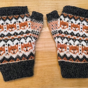 May include: A pair of fingerless gloves with a brown, white and black knit pattern featuring a repeating fox design.