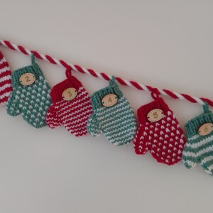 May include: A string of knitted mittens with numbers 1 to 7 on them. The mittens are red and white striped, green and white striped, or red with white polka dots. The mittens are strung on a white and red twine.