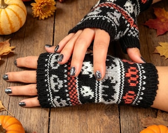 May include: A pair of fingerless gloves featuring a black, white, and orange knit pattern with repeating skull and crossbones motifs. The gloves have ribbed cuffs at the top and bottom, covering the hands while leaving the fingers exposed.