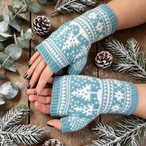 May include: A pair of fingerless gloves in a light blue and white colour scheme, featuring a knit pattern of stylised trees and geometric shapes. The gloves have a ribbed cuff at the wrist and an opening for the thumb, covering the hand.