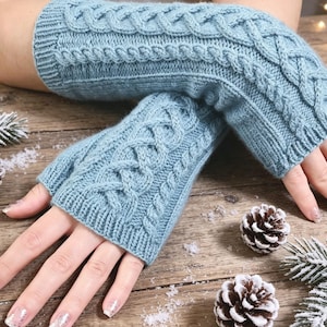 May include: A pair of light blue fingerless gloves featuring a textured cable knit pattern. The gloves have a ribbed cuff at the wrist and extend to cover the forearm, showcasing a consistent knit design throughout the entire length of the garment.