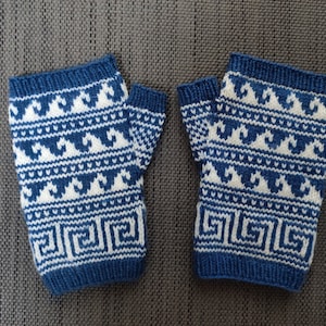 May include: A pair of blue and white knitted fingerless gloves. The gloves feature a repeating wave and geometric pattern. The cuffs and top edges are a solid blue. The gloves are displayed on a gray surface.