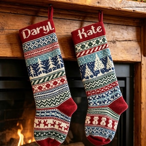 May include: Two red, white, and blue knit Christmas stockings featuring intricate patterns of pine trees, reindeer, and snowmen. The left stocking is personalized with the name Daryl, and the right stocking is personalized with the name Kate.