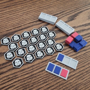 May include: A collection of Star Wars-themed game pieces. The set includes black and white hexagonal tiles with Stormtrooper faces, gray rectangular pieces, and blue and pink square blocks. The pieces are arranged on a wooden surface.