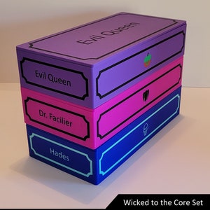 May include: Four stacked boxes with different colored lids and labels. The top box is purple with the label "Evil Queen" and a strawberry icon. The second box is pink with the label "Dr. Facilier" and a voodoo icon. The third box is blue with the label "Hades" and a skull icon. The boxes are labeled "Wicked to the Core Set".