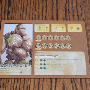 May include: A brown card game board with a stone creature illustration. The card features a character called "Vital Strength of the Earth" with special rules and innate powers. The card has a growth pick one option, a card play option, and a gift of strength option. The card has a cost of 2 energy.
