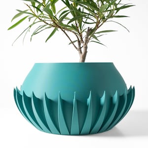 Peut inclure: Pot de fleurs turquoise avec un design unique et plissé. Le pot est fait d'un matériau lisse et mat et présente une large ouverture ronde. Une petite plante verte pousse à l'intérieur du pot.