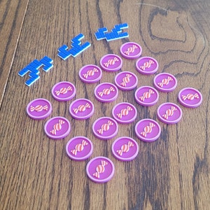 May include: A set of 20 pink and white candy tokens with a swirl design. The tokens are arranged in a semi-circle on a wooden surface. The word "FREE" is spelled out in blue tiles.