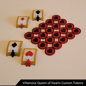 May include: A set of custom game tokens featuring a black spade, a red diamond, a red heart, and a black heart. There are also 20 red tokens with black hearts on them.